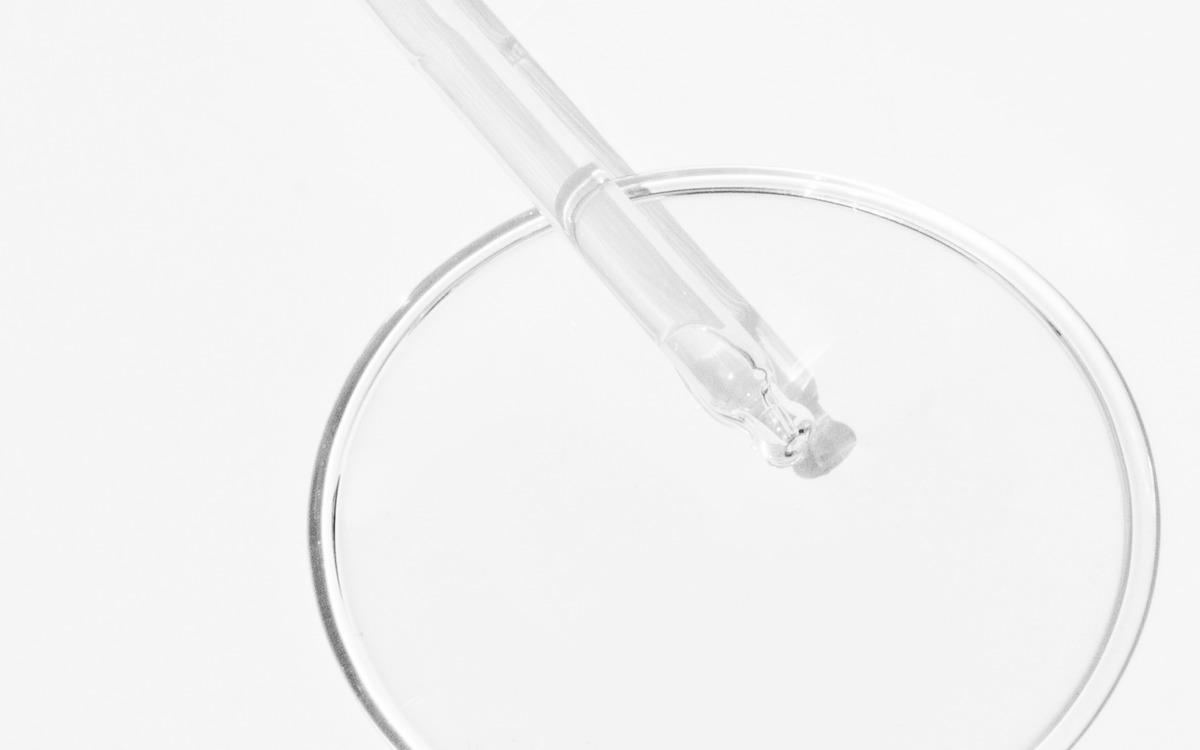 Eine Pipette steht über einer klaren Petrischale auf einem weißen Hintergrund.