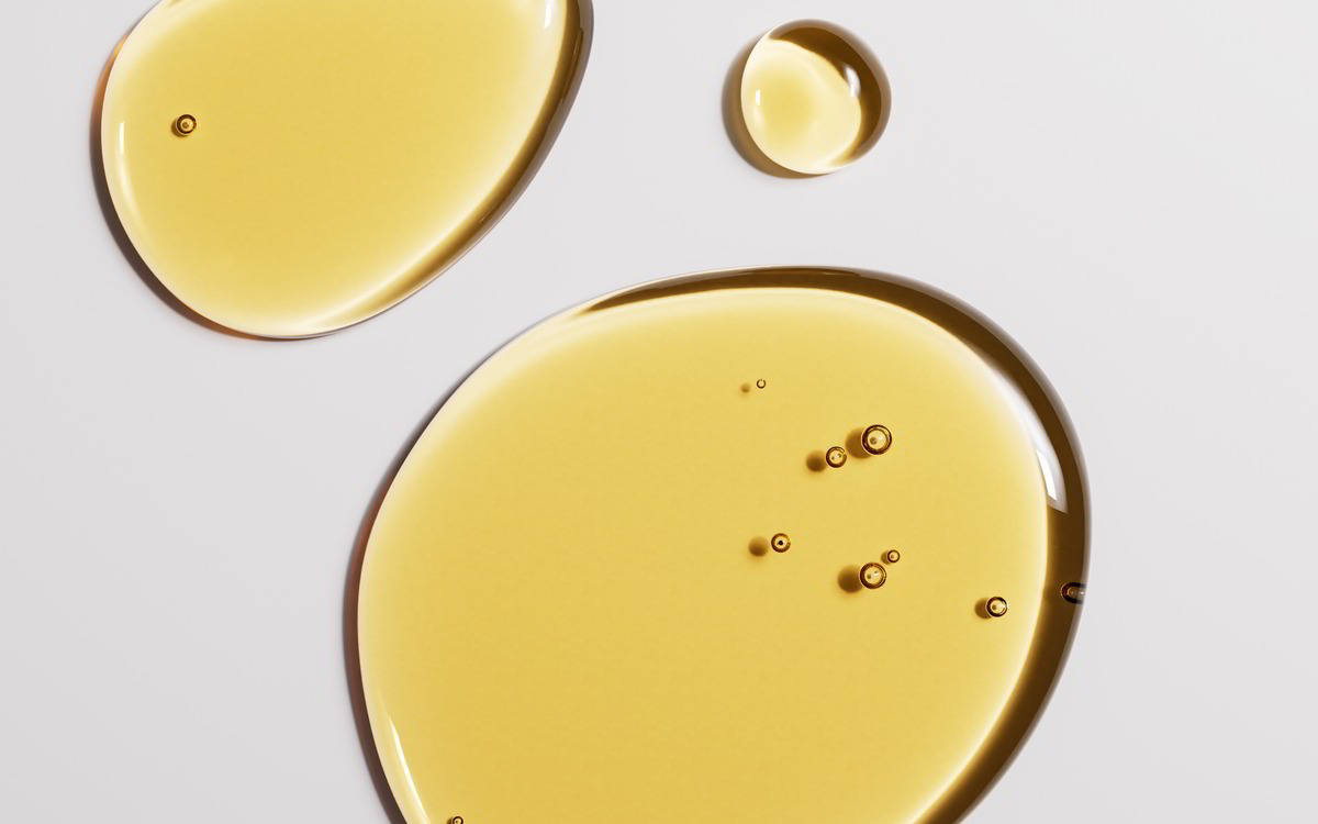 Transparente, gelbe Flüssigkeitstropfen auf einem hellen Hintergrund, mit kleinen Bläschen darin.